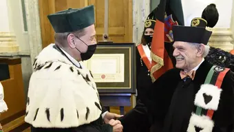Na zdjęciu Rektor Jerzy Lis gratuluje Profesorowi Alberto Sangiovanni. Obaj Panowie ubrani są w stroje ceremonialne. Rektor ubrany jest w togę i biret koloru zielonego oraz kołnierzem z gronostajów, natomiast profesor Sangiovanni ma na sobie togę i biret w kolorze czarnym.