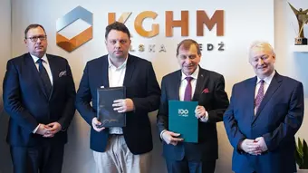 czterech uczestników spotkania stoi w rzędzie, za nimi ściana z logo KGHM