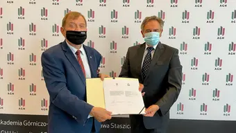 Rektor Jerzy Lis oraz profesor Janusz Szmyd wspólnie trzymają otwartą teczkę z widocznymi dwoma dokumentami.