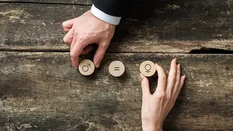 Zdjęcie przedstawiające dwie dłonie, damską i męską układające na stole drewniane klocki z symbolami płci. Pomiędzy nimi widać trzeci klocek z symbolem znaku równości.