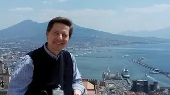 Zdjęcie przedstawia w centralnej części mężczyznę na tle panoramy miasta Neapolu (w tle widoczny wulkan - Wezuwiusz, po prawej - widoczna zatoka i morze).