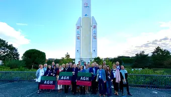 Zdjęcie przedstawia blisko trzydziestoosobową grupę pracowników AGH. W tle widać białą rakietę kosmiczną.