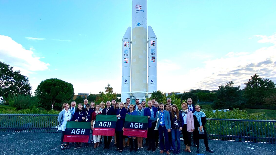 Zdjęcie przedstawia blisko trzydziestoosobową grupę pracowników AGH. W tle widać białą rakietę kosmiczną.
