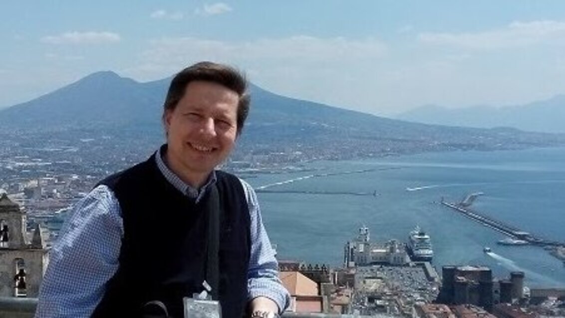 The photo shows a man with the panorama of Naples behind his back; Vesuvius volcano is in the background; on the right there is a gulf and the sea.