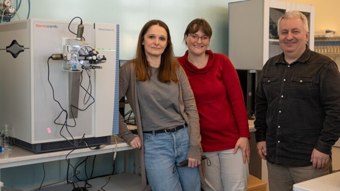 Zdjęcie przedstawia dwie kobiety oraz mężczyznę, którzy stoją obok siebie w rzędzie w laboratorium