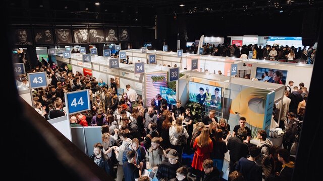 Widok z góry na halę targów. Pośród stoisk wystawców krąży tłum odwiedzających. 