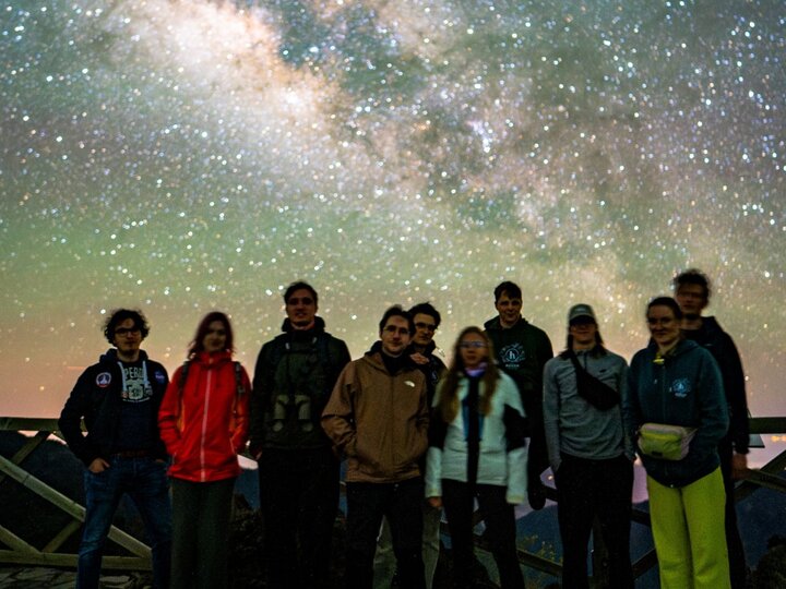 A group of people standing against a starry sky at night.