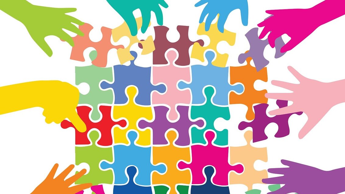 Grafika przedstawiająca rożnokolorowe dłonie układające różnokolorowe puzzle.