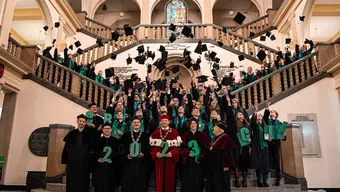 Image of university authorities and university graduates throwing their birettas up in the air while standing on the stairs in the main building of the university