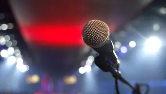 Zdjęcie mikrofonu na statywie, w tle rozświetlona sala