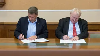 Na zdjęciu moment podpisania umowy przez obie strony - przy stole dwóch mężczyzn, podpisujących dokumenty. Zdjęcie wykonane w sali konferencyjnej AGH.