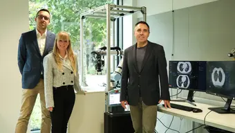 Na zdjęciu trzy osoby (twórcy systemu) w laboratorium, stoją przy urządzeniu do analizy obrazów tomografii komputerowej.