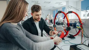 Two students working with a Helmholtz coil in a physics lab, using scientific instruments.