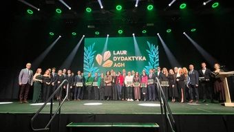 Zdjęcie grupowe: kilkadziesiąt osób, w tym wszyscy nominowani, stoi na scenie podczas gali Laur Dydaktyka AGH; za nimi duży ekran z logo wydarzenia i zieloną dekoracją świetlną.