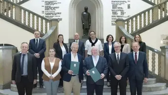 A group of people in business attire standing on a decorative staircase in front of a black monument of Stanisław Staszic.