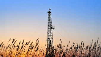 Szyb wiertniczy wystający ponad łany zboża widoczny na tle wieczornego nieba