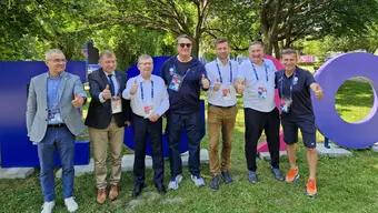 Grupowe zdjęcie - obok siebie stoi siedmiu mężczyzn (drugi od lewej - Rektor AGH prof. Jerzy Lis, pierwszy z prawej - Robert Korzeniowski). Zdjęcie wykonane na Miasteczku AGH - w Wiosce Zawodniczej. Za plecami mężczyzn kolorowe litery ustawione na trawniku.