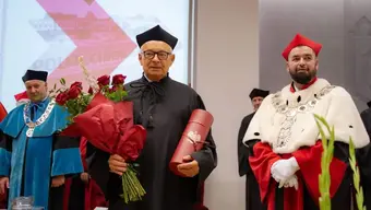 Na zdjęciu prof. Janusz Kowal w czarnej todze i birecie, tuż po nadaniu tytułu. W rękach trzyma kwiaty oraz tubę z pamiątkowym dyplomem. Obok niego, po prawej stronie, stoi Rektor PBŚ w stroju reprezentacyjnym. Zdjęcie wykonane podczas uroczystości.
