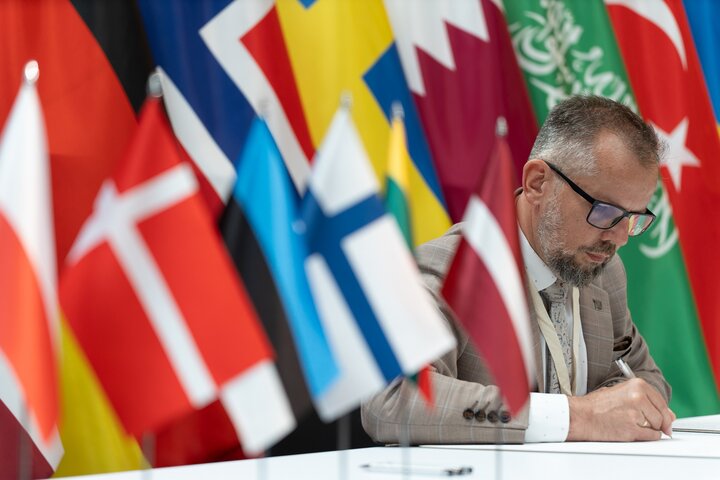 Professor Krzysztof Mendrok pictured signing a document surrounded by flags of Baltic countries.