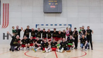 Grupowe zdjęcie drużyny piłkarzy ręcznych AZS AGH. Na roześmianych twarzach zawodników maluje się radość i duma. Część zawodników ma uniesione w górę ręce w geście zwycięstwa. Zdjęcie wykonane w hali sportowej. Zawodnicy w pierwszym rzędzie siedzą na parkiecie, w drugim - stoją.