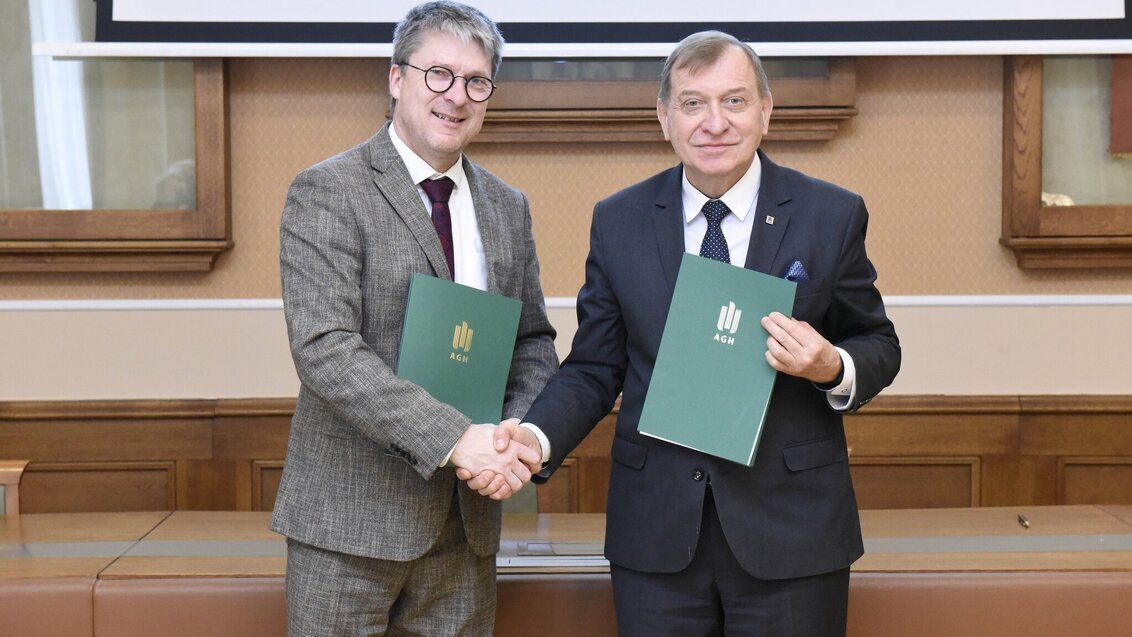 Dwóch ubranych w garnitury mężczyzn. Po lewej dyrektor INSA CVL, a po prawej Rektor AGH Jerzy Lis. Przed sobą trzymają teczki z logo AGH. 