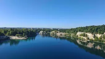 Błękitna tafla jeziora, wokół którego rozpościerają się wokół skałki z zielonymi drzewami.