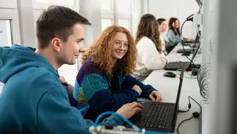 An image of a group of students sitting in a laboratory in front of laptops. The main focus of the photograph is on a pair of smiling students.