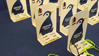 Na stole znajdują się ustawione statuetki w kształcie pingwina z logotypami 