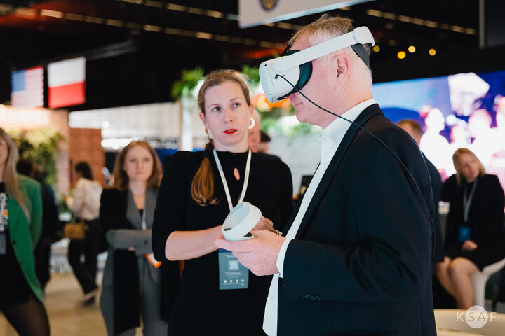 A man wearing VR goggles and a woman standing next to him with a serious expression on her face.