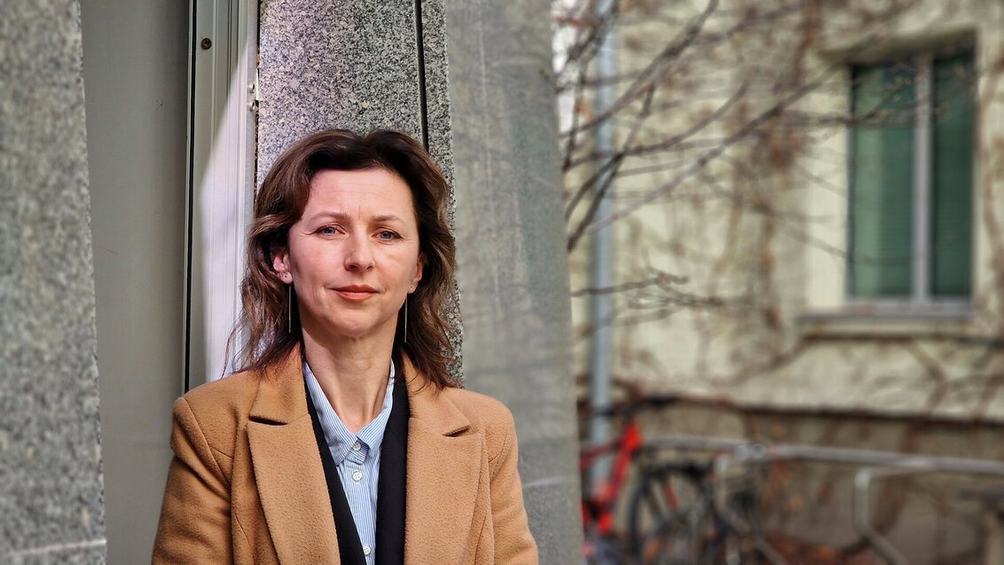 Image of a woman wearing camel coat standing against a building