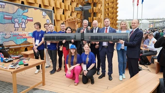 Zdjęcie delegacji AGH, NAWA, FRSE i MNiSW z młodymi wynalazcami prezentująca drona podczas EXPO przed polskim pawilonem.