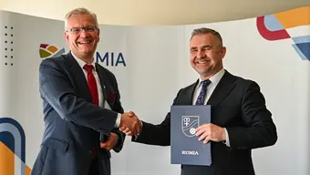Dwóch sygnatariuszy umowy ściska swoje prawe dłonie, w lewych trzymając podpisane dokumenty.