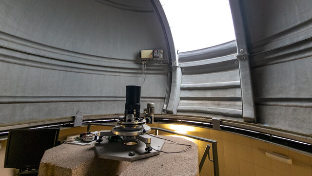 The interior of an observatory with a partially open dome and a telescope.