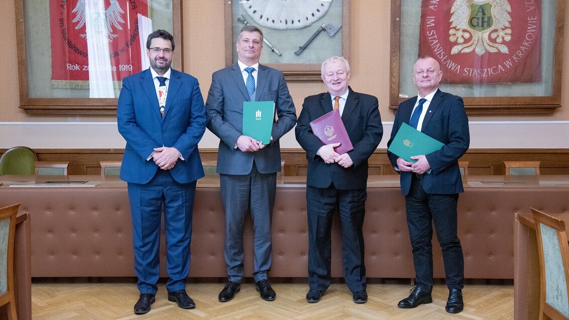 The signers of the agreement. Four men in suits holding document folders. The photo was taken in a conference room.