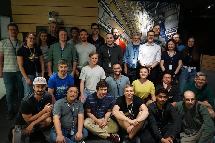 A group of people, some standing, some sitting, posing in front of a large scientific poster or mural.