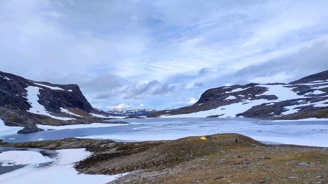 Obóz namiotowy naukowców AGH. W centralnej części jezioro Láddejávrre, nad jeziorem cztery namioty. W tle widać góry częściowo pokryte śniegiem.