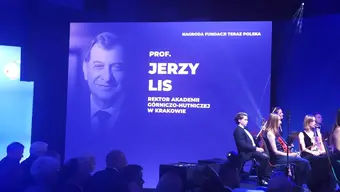Gala wręczenia nagród. Na scenie ekran z napisem: "Prof. Jerzy Lis, Rektor Akademii Górniczo-Hutniczej w Krakowie". Na scenie siedzi orkiestra smyczkowa.