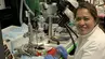 Photograph of a researcher working at a microscope-assisted experimental workstation equipped with surgical and imaging instruments.