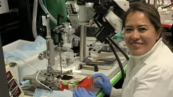 Dr Gloria Lesly Jimenez Miranda podczas pracy w laboratorium badawczym. Naukowczyni w białym fartuchu siedzi przy stanowisku wyposażonym w specjalistyczną aparaturę laboratoryjną i mikroskop.