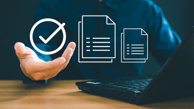 Grafika dekoracyjna: postać siedząca przed laptopem z dłonią wskazującą na ikonki symbolizujące cyfrowy obieg dokumentów.