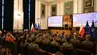 The photo was taken in the AGH UST Assembly Hall. Participants sitting in rows on chairs, including numerous people in military uniforms. At the lectern, Marcin Ociepa. Behind him, on two large screens, a presentation.