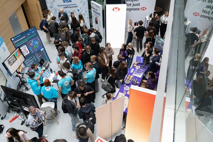 Crowded indoor event with many people gathered around company booths and displays.