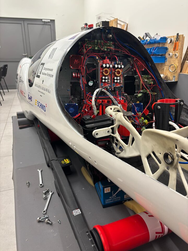 The image shows the interior of a sleek white vehicle, with exposed electronics and tools in a garage setting.