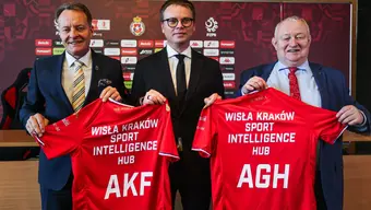 Trzech mężczyzn w garniturach stoi obok siebie, trzymając w dłoniach czerwone koszulki sportowe z napisami „Wisła Kraków Sport Intelligence Hub” oraz inicjałami „AKF” i „AGH”.