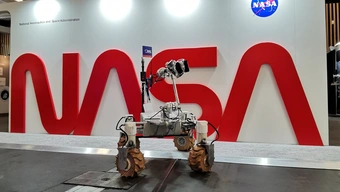 The Kalman robot – a platform with huge and widely spaced off-road wheels and research equipment; it stands by a white wall with a large red logo of NASA.
