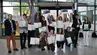 A group of students holding diplomas and financial prizes in a glassed-in interior.