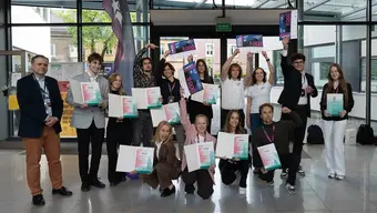 A group of students holding diplomas and financial prizes in a glassed-in interior.