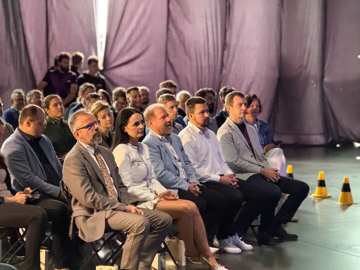 An audience of a dozen or so people sitting on chairs in an industrial-style interior.