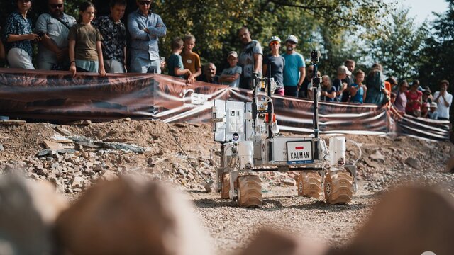 A Martian rover during the European Rover Challenge on the AGH University campus. The robot is moving along a Marsyard watched by spectators.
