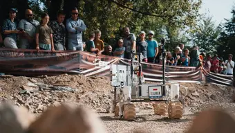 Łazik marsjański podczas zawodów European Rover Challenge na kampusie AGH. Robot porusza się po marsjańskim torze testowym. Obserwuje go publiczność.
